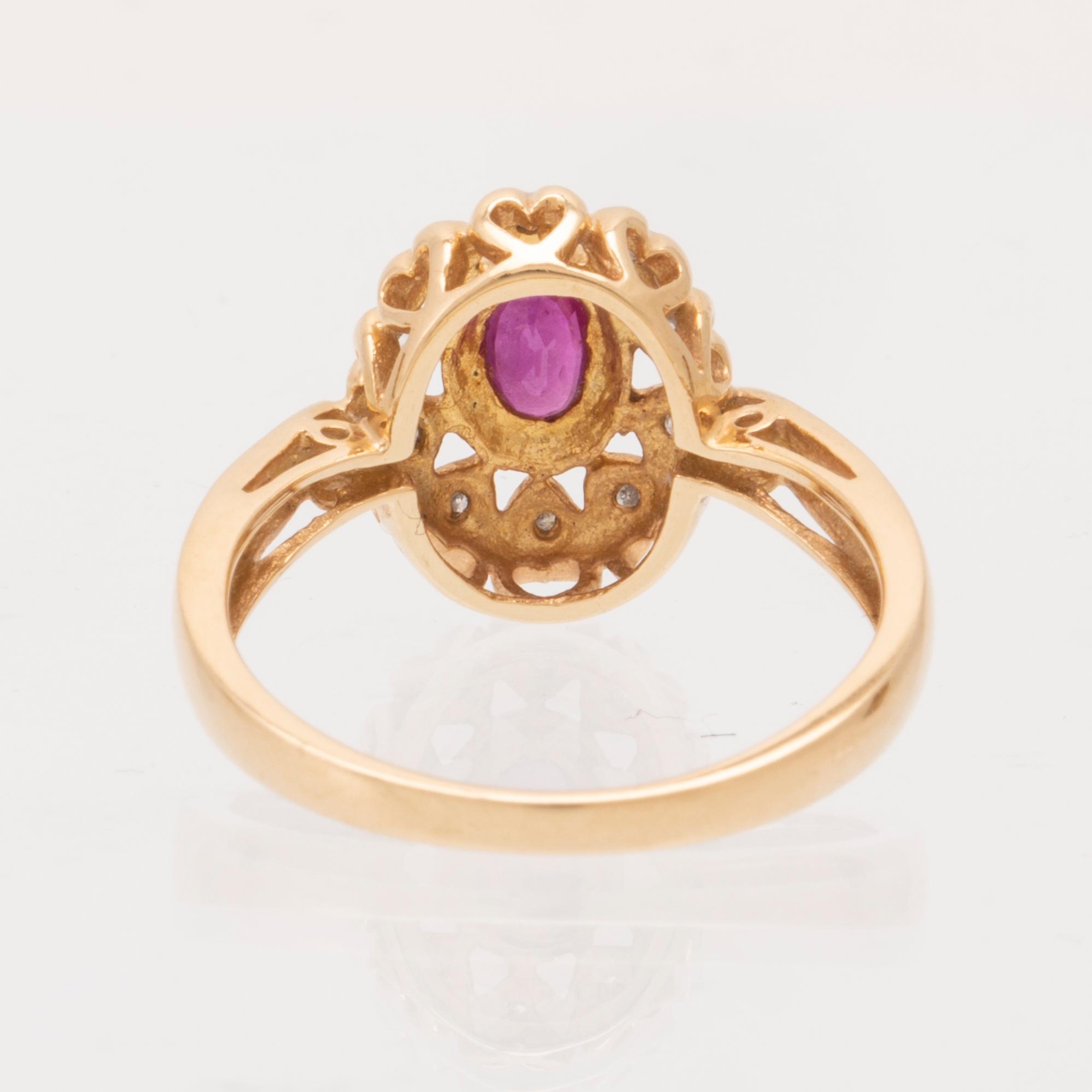 An 18K gold ring set with an oval brilliant cut ruby and round brilliant cut diamonds.