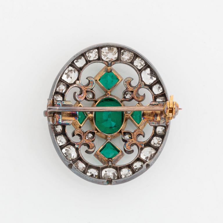 A gold and silver brooch set with faceted emeralds and old- and rose-cut diamonds.