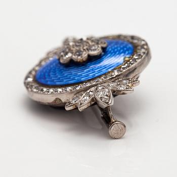 An palladium, silver and gold brooch with a metal pin, enamel decor and diamonds ca. 1.38 ct in total.