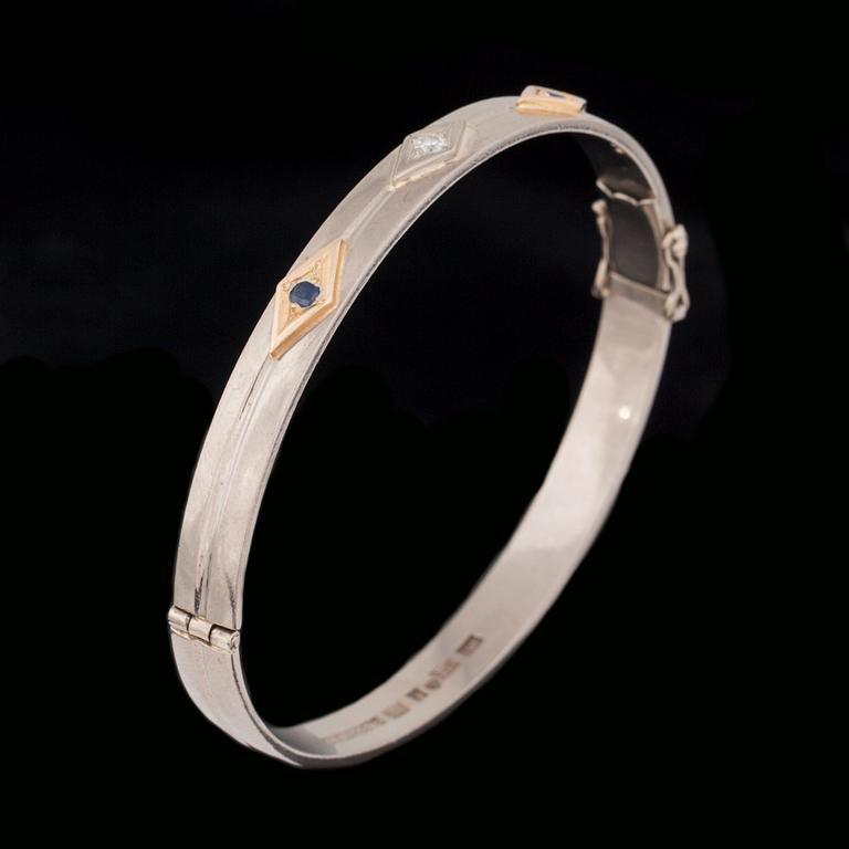 ARMRING, 18 k vitguld med briljantslipad diamant ca 0.05 ct samt 2 fasettslipade safirer. Vikt ca 33 g.