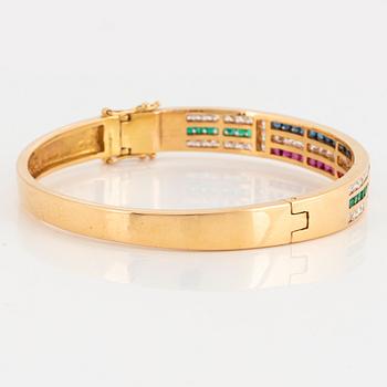 An 18K gold bangle set with round brilliant-cut diamonds, sapphires, emeralds and rubies.