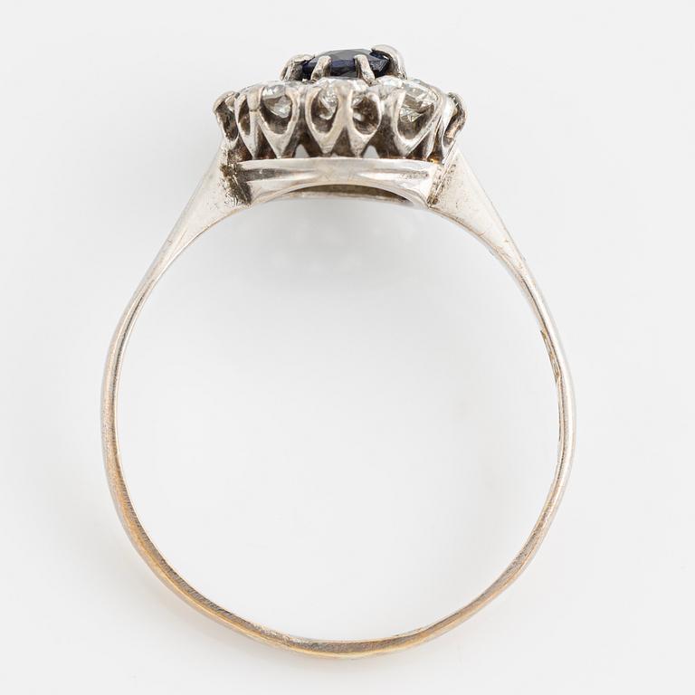An 18K white gold ring set with a synthetic sapphire and round brilliant-cut diamonds.