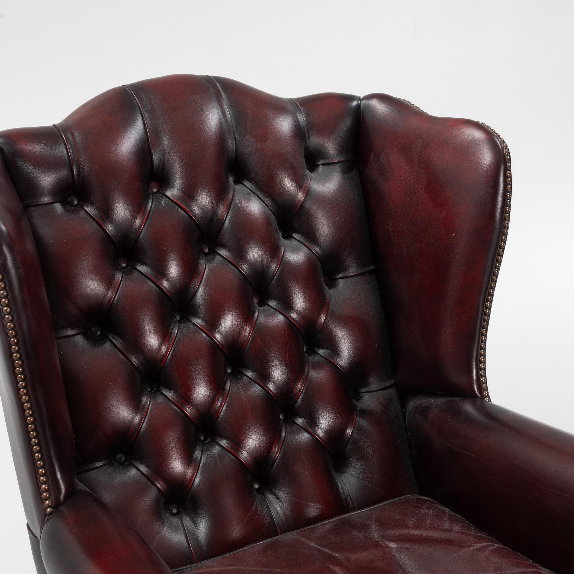 A leather upholstered wingback chair with stool. end of the 20th Century.