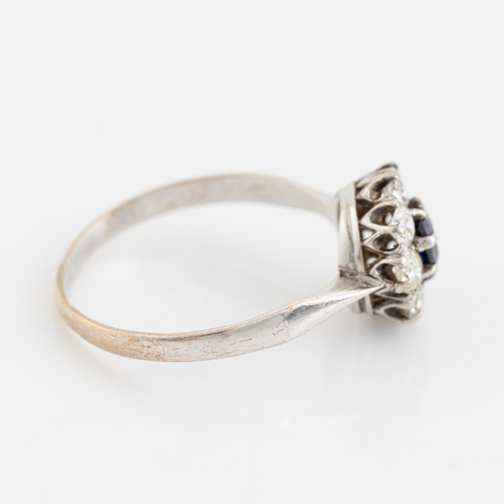An 18K white gold ring set with a synthetic sapphire and round brilliant-cut diamonds.