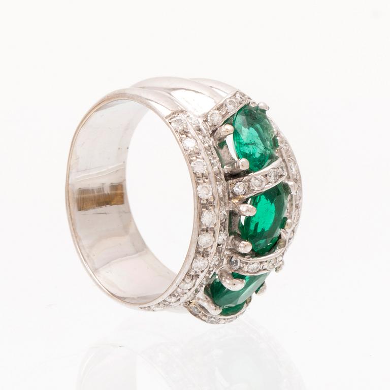 An 18K white gold ring set with oval cut emeralds and round brilliant cut diamonds.