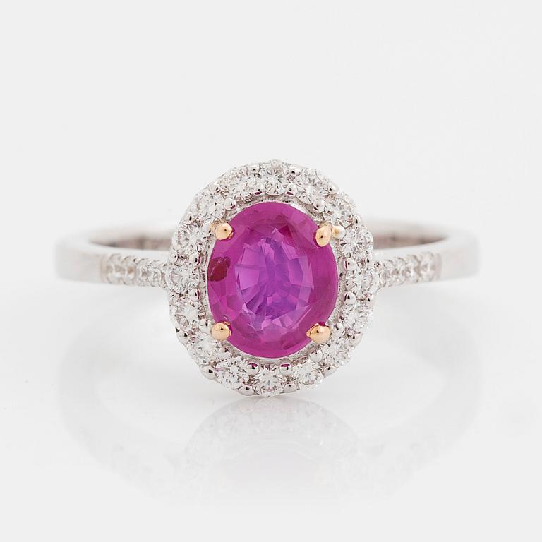 An 18K white gold ring set with a faceted pink sapphire and round brilliant-cut diamonds.