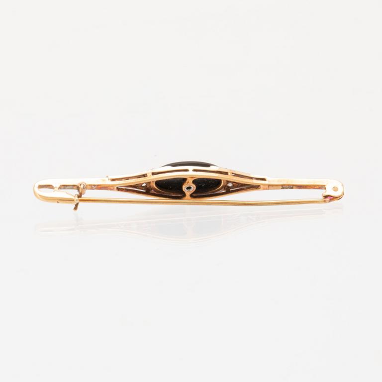 A 14K white and red gold brooch set with round brilliant-cut and rose-cut diamonds and a black stone.