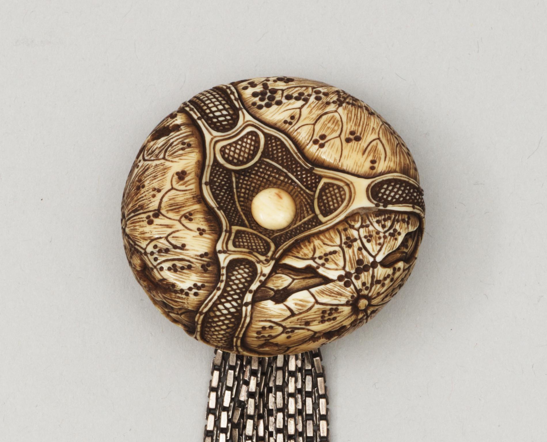 A Japanese embroided tabakoire with a kanamono in the shape of two tigers, a metal chain that holds a carved ivory manjû, second half of 19th Century. Signed.