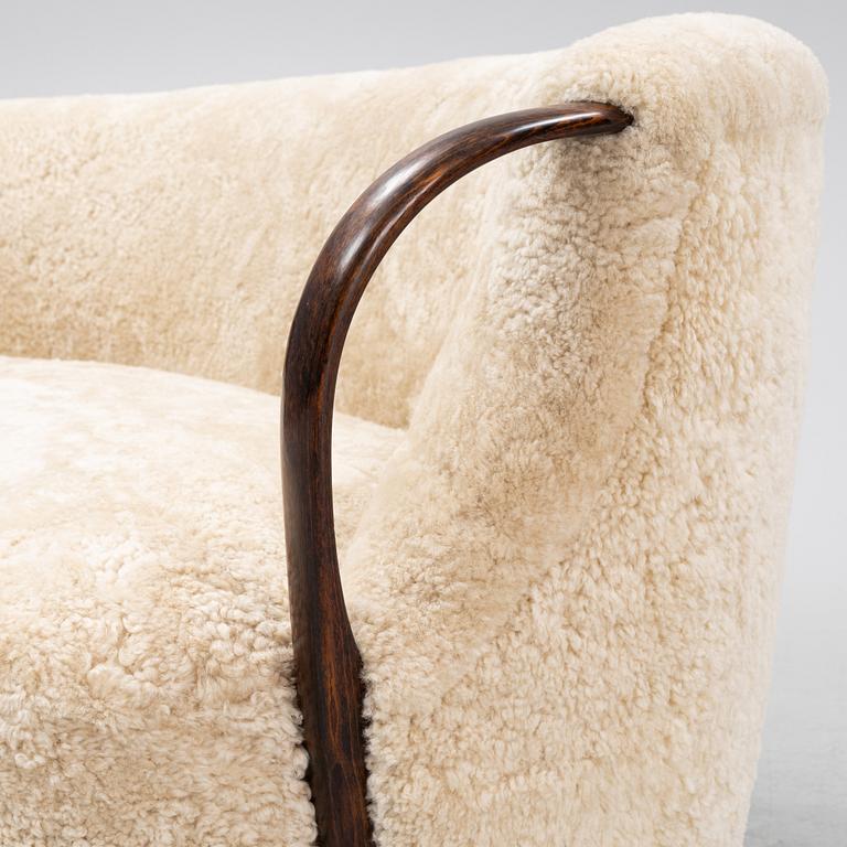 A curved sofa attributed to Viggo Boesen with new sheepskin upholstery and stained beech tree armrests.