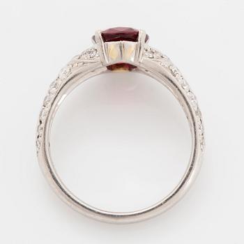 A platinum ring set with a faceted ruby and round brilliant-cut diamonds.