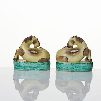 A pair of green, yellow and aubergine glazed biscuit figures of recumbent horses, Qing dynasty.