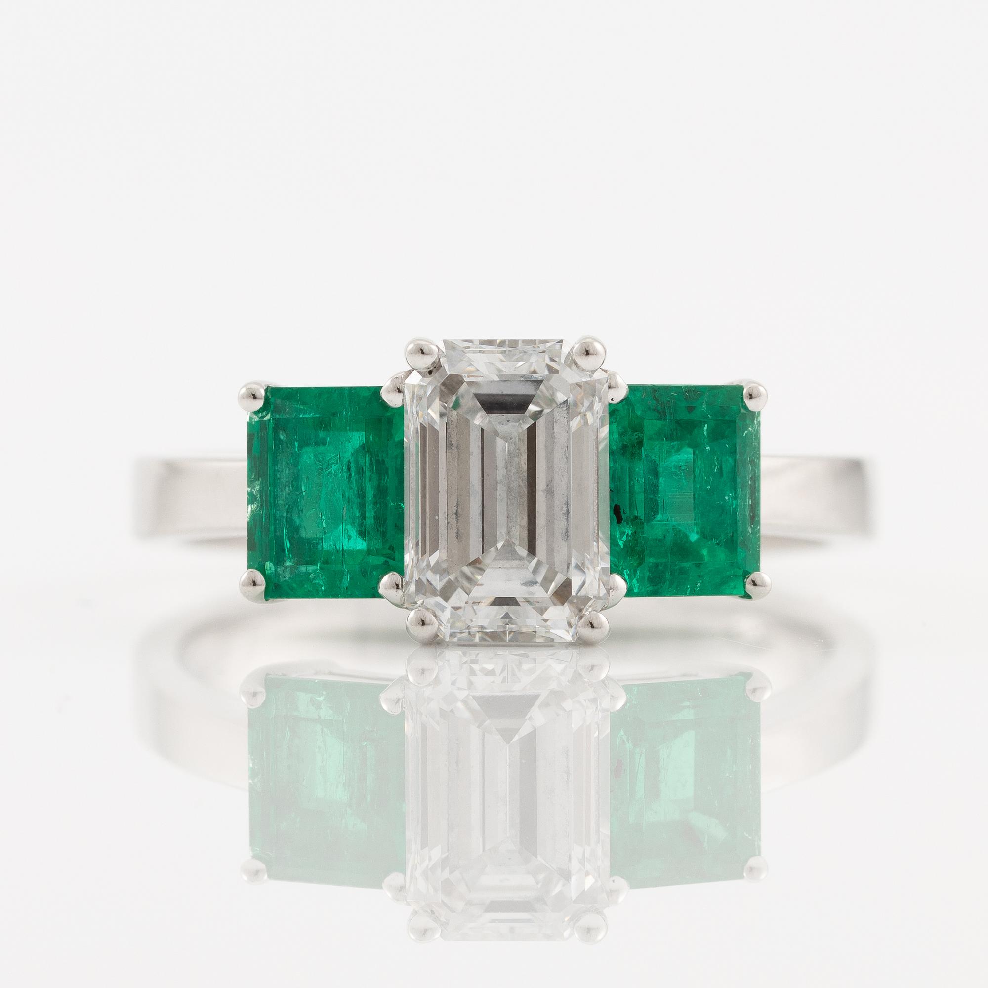 An 18K white gold ring set with an emerald-cut diamond and two step-cut emeralds.