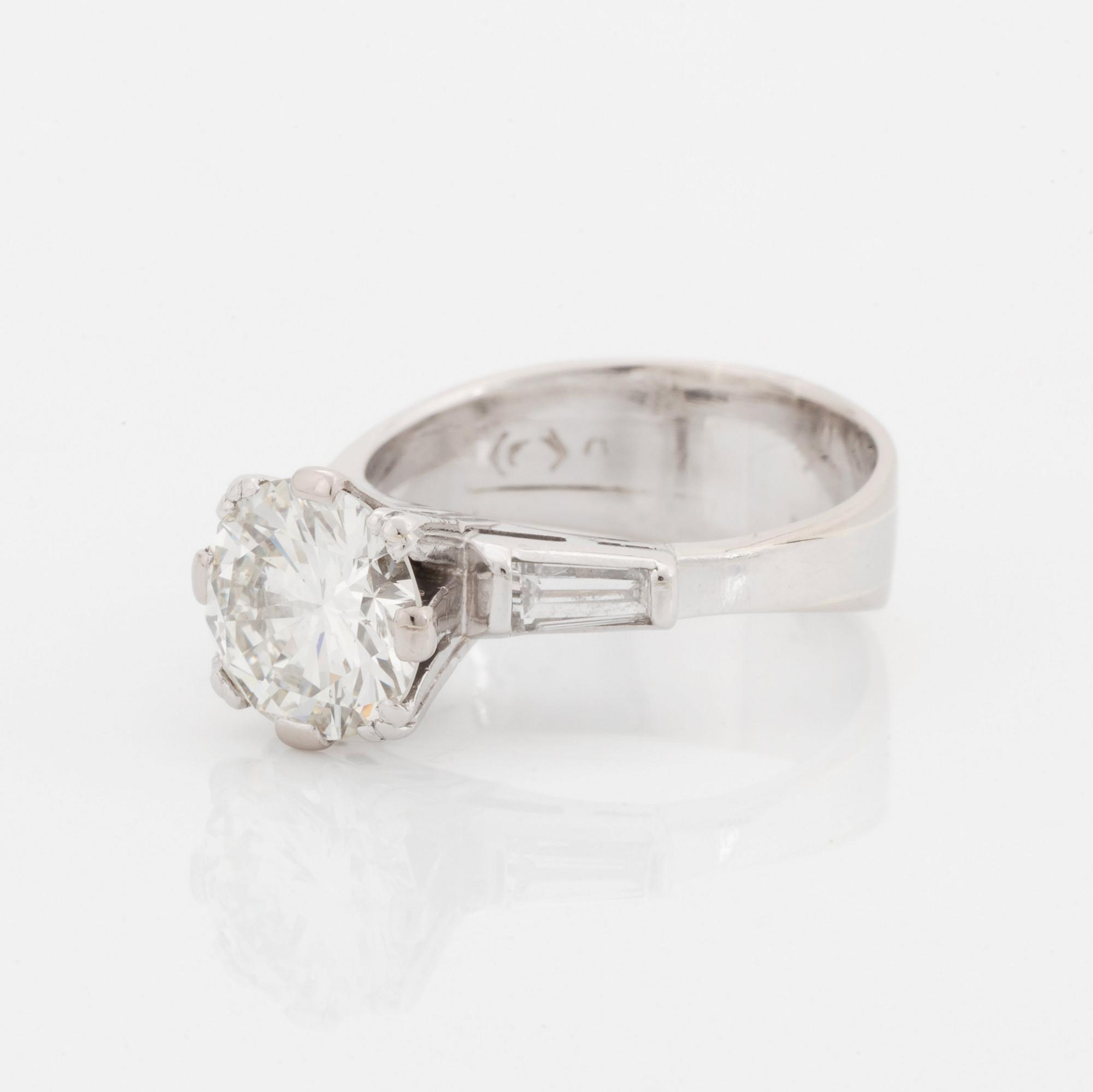 An 18K white gold ring set with a round brilliant-cut diamond and two tapered baguette-cut diamonds.