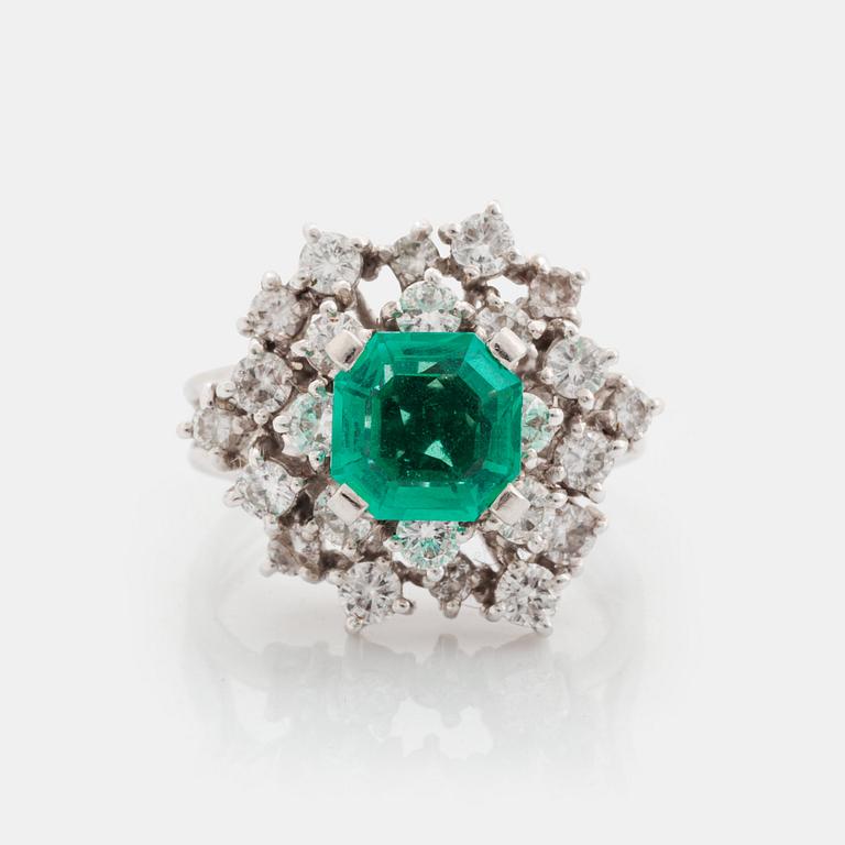 A platinum ring set with a faceted emerald and round brilliant-cut diamonds.