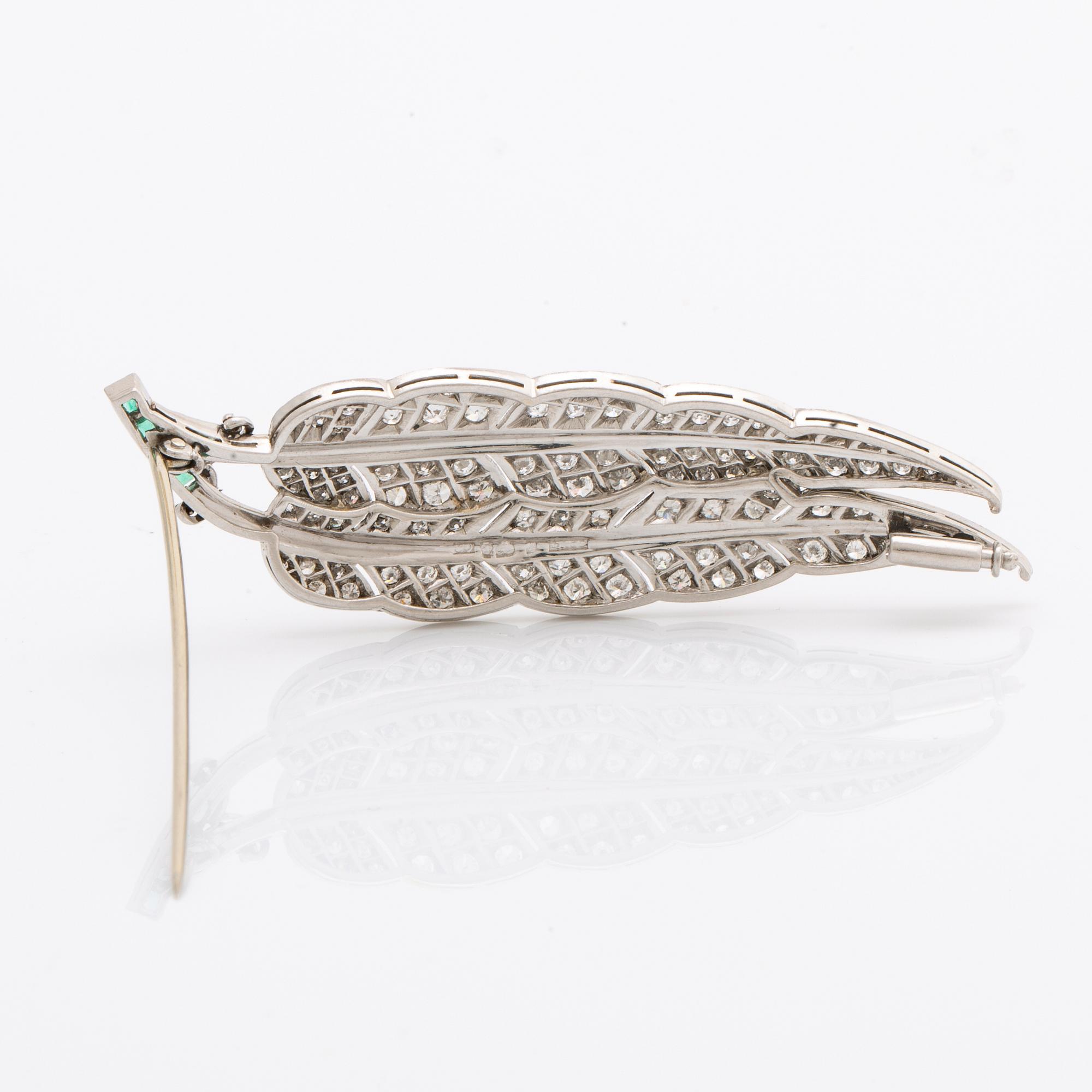 A platinum brooch set with round brilliant-cut diamonds and emeralds.