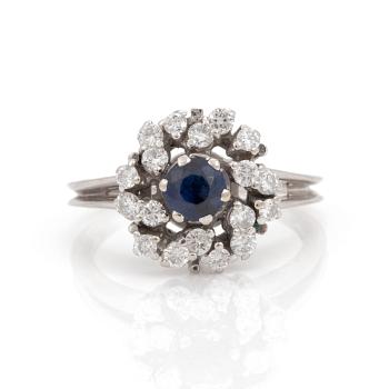 A ring set with a round, mixed-cut synthetic sapphire and round, brilliant-cut diamonds.