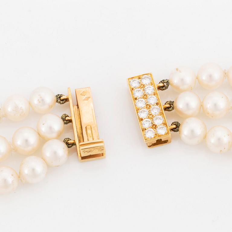 A Cartier triple strand cultured pearl necklace with an 18K gold clasp set with round brilliant-cut diamonds.