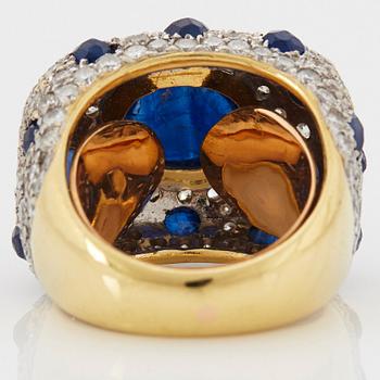 An 18K gold ring set with a cabochon-cut sapphire and round brilliant-cut diamonds and faceted sapphires.