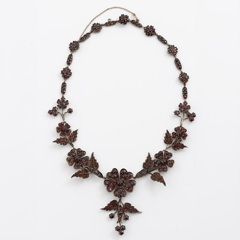 Garniture, necklace/bracelet and earrings in silver with garnets in the form of floral motifs, around the turn of the 20th century.