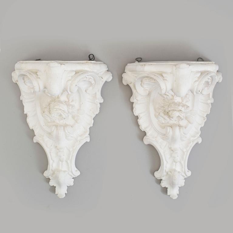 A pair of consoles and a set of three decor-elements, plaster, 20th century.