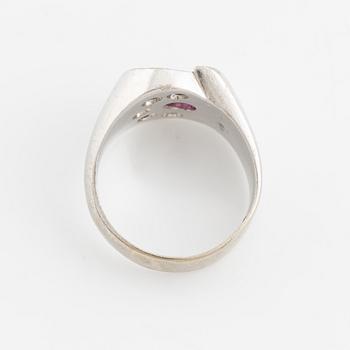 An 18K white gold ring set with a faceted ruby and round brilliant-cut diamonds.