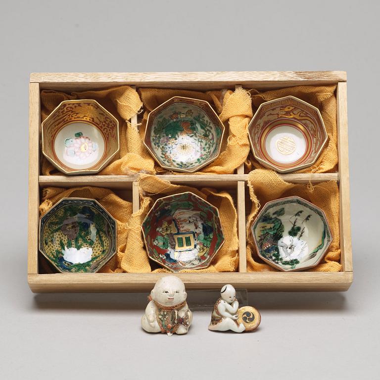 A set of two Japanese figures and a set of six cups in a wooden box, early 20th Century.