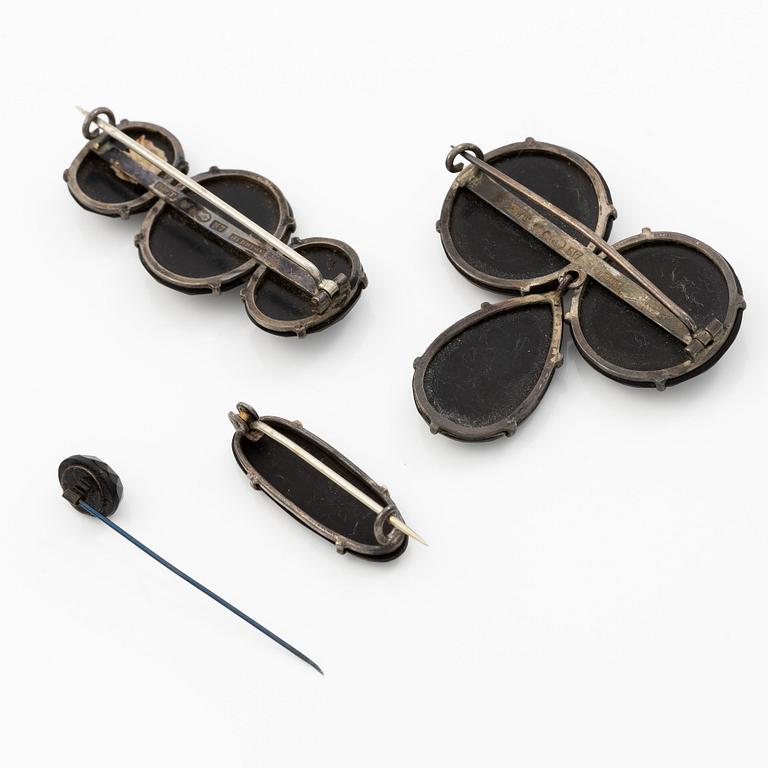 Samling smycken silver med svarta fasettslipade stenar, tre broscher, hattnål, medaljong och armband.