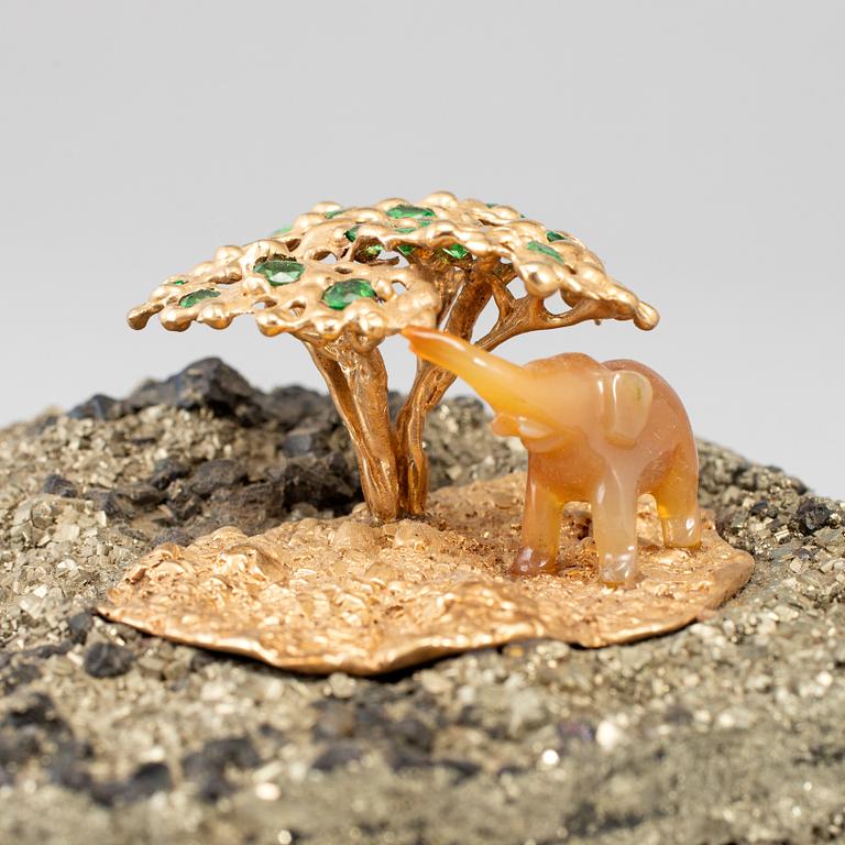 A sculpture of an agate elephant under a gilt three with inlays of tsavorites on rock formation, unmarked, 20th Century.