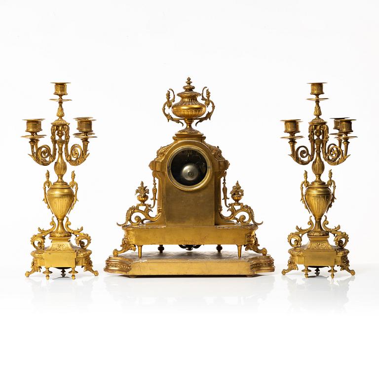 A mantle clock and a pair of candelabra, Louis XVI style, ca 1900.