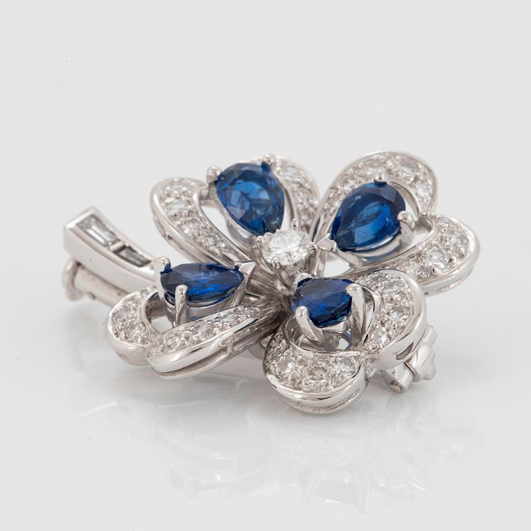 A Meister brooch in 18K white gold set with faceted sapphires, a round brilliant-cut diamond.