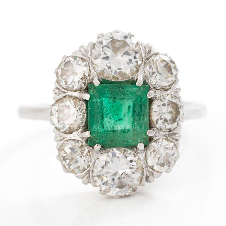 18K white gold ring set with a faceted emerald and round brilliant-cut diamonds.