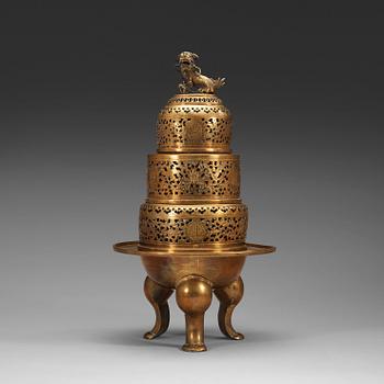 A four-part brass tripod censer, pierced sections with lotus scrolls and a fo-dog finial, late Qing dynasty (1644-1912).