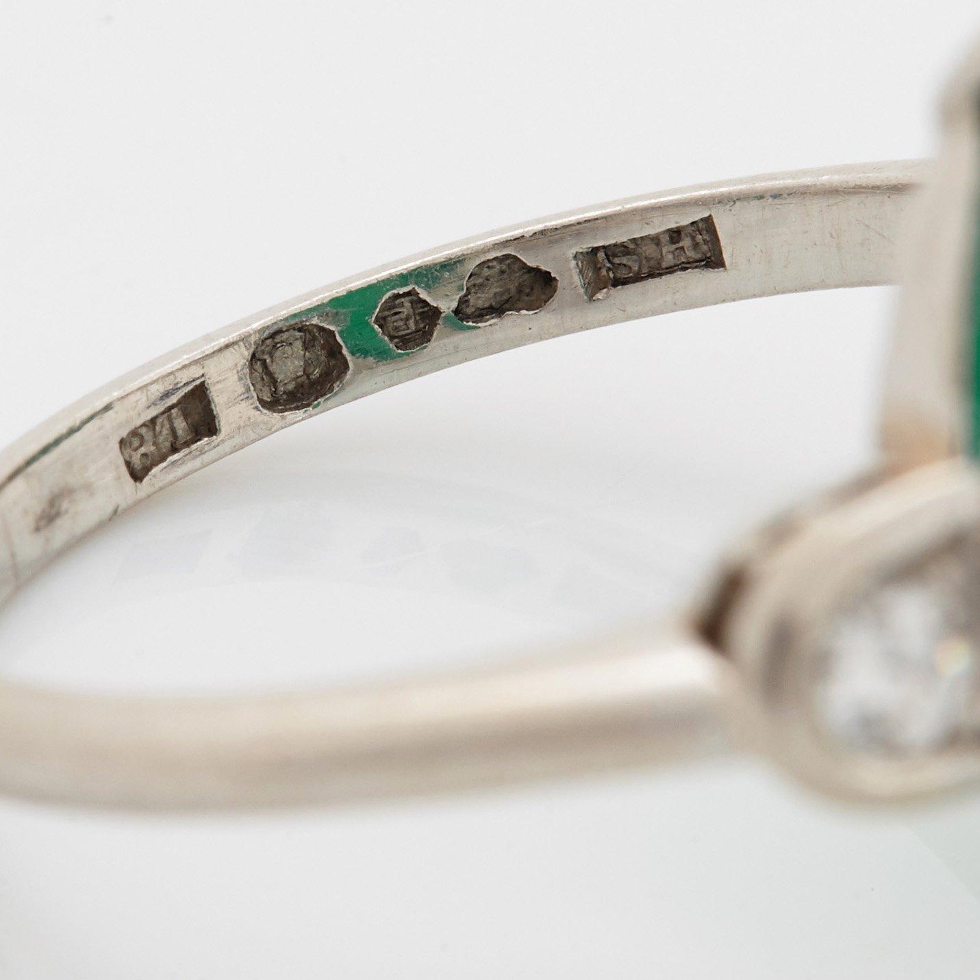 A platinum ring set with a cabochon-cut emerald and round brilliant-cut diamonds.