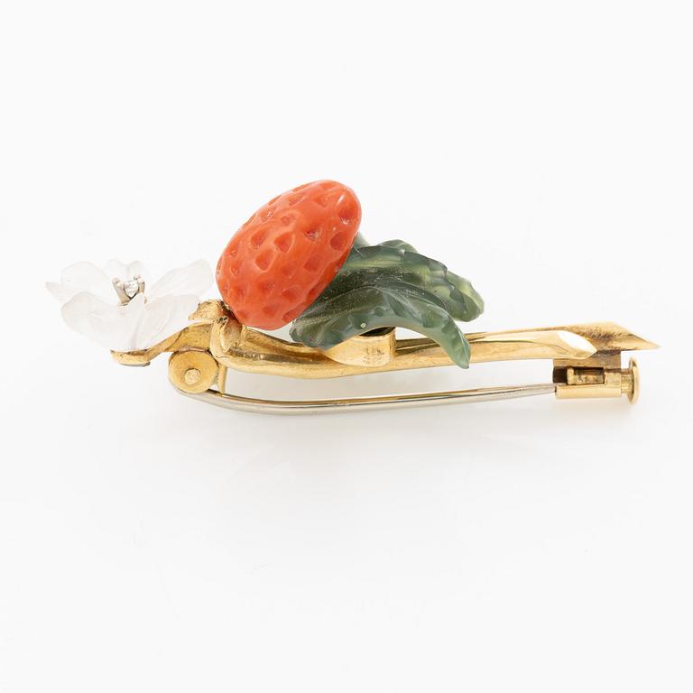 A flower brooch 18K gold with coral, rock crystal, a green stone likely nephrite, and a round brilliant-cut diamond.