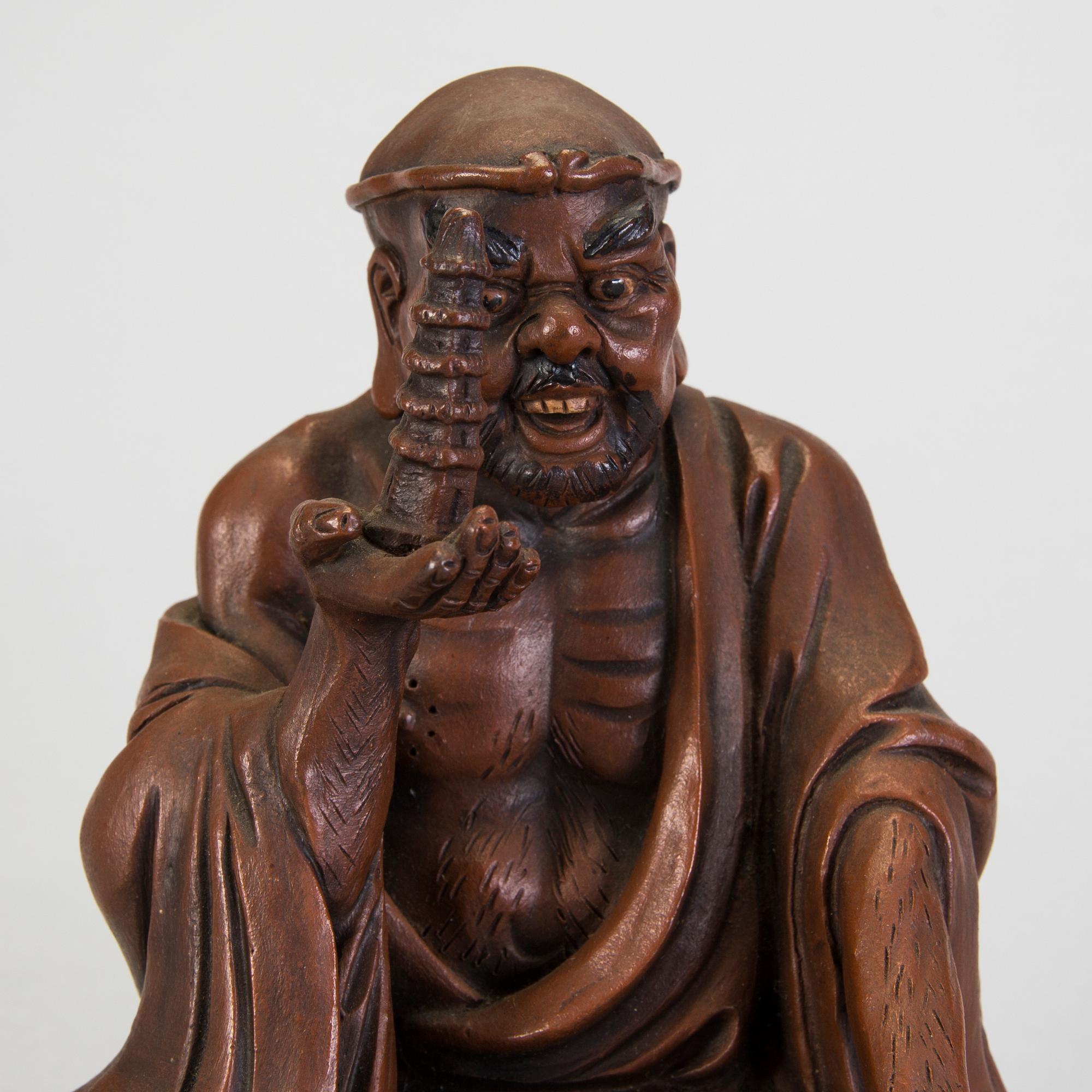 A Japanese earthenware seated figure of a man holding a pagoda, 20th century.