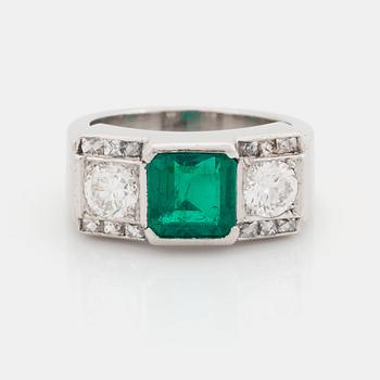 A platinum ring set with a step-cut emerald and round brilliant- and step-cut diamonds.