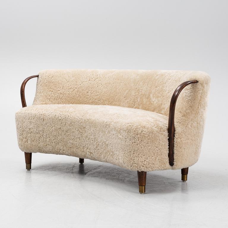 A curved sofa attributed to Viggo Boesen with new sheepskin upholstery and stained beech tree armrests.