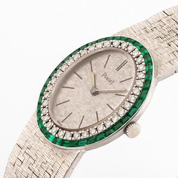 A Piaget 18K white gold wrist watch set with round brilliant-cut diamonds and step-cut emeralds.