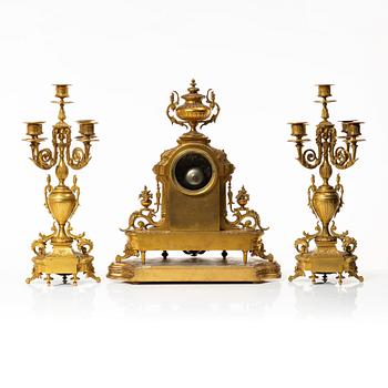 A mantle clock and a pair of candelabra, Louis XVI style, ca 1900.