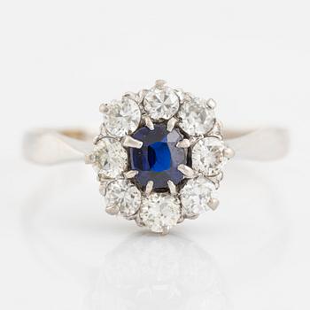 An 18K white gold ring set with a synthetic sapphire and round brilliant-cut diamonds.