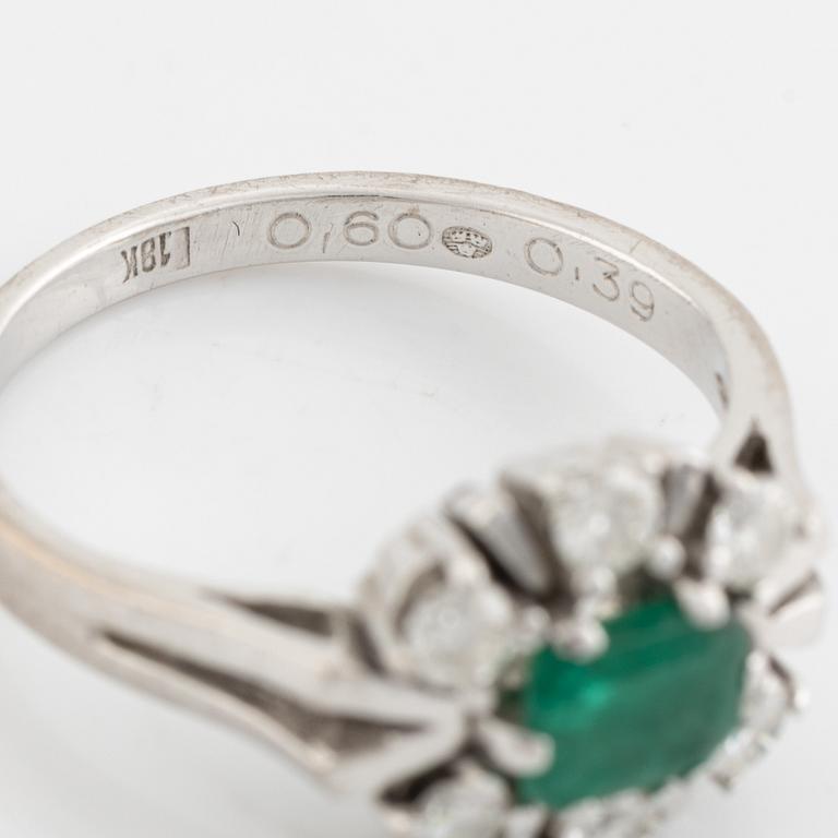 An 18K white gold ring set with a faceted emerald and round briliiant-cut diamonds.