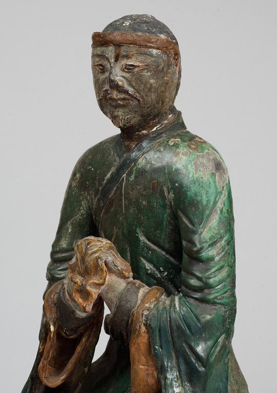 A green and yellow glazed pottery figure of a guardsman, seated on a postament, Ming dynasty.