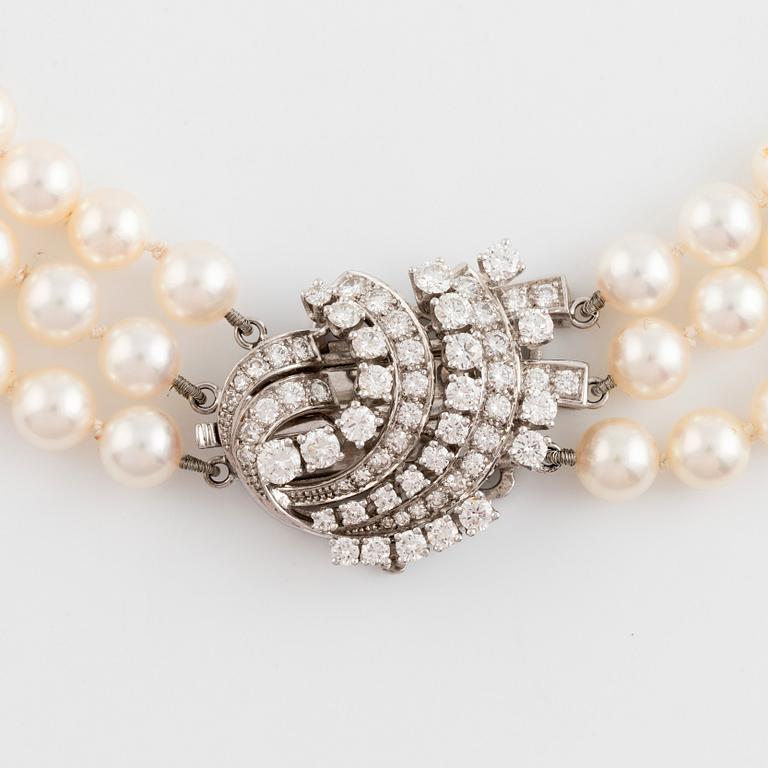 A three strand cultured pearl necklace with an 18K gold clasp set with round brilliant-cut diamonds.