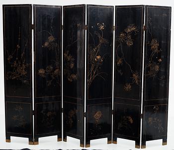 A chinese black lacquer six-panel screen, early 20th Century, with figures in gardens, inlays of carved mother of pearl, coloured bone, tree, and different stones. Back of panels with flowers painted in gold.