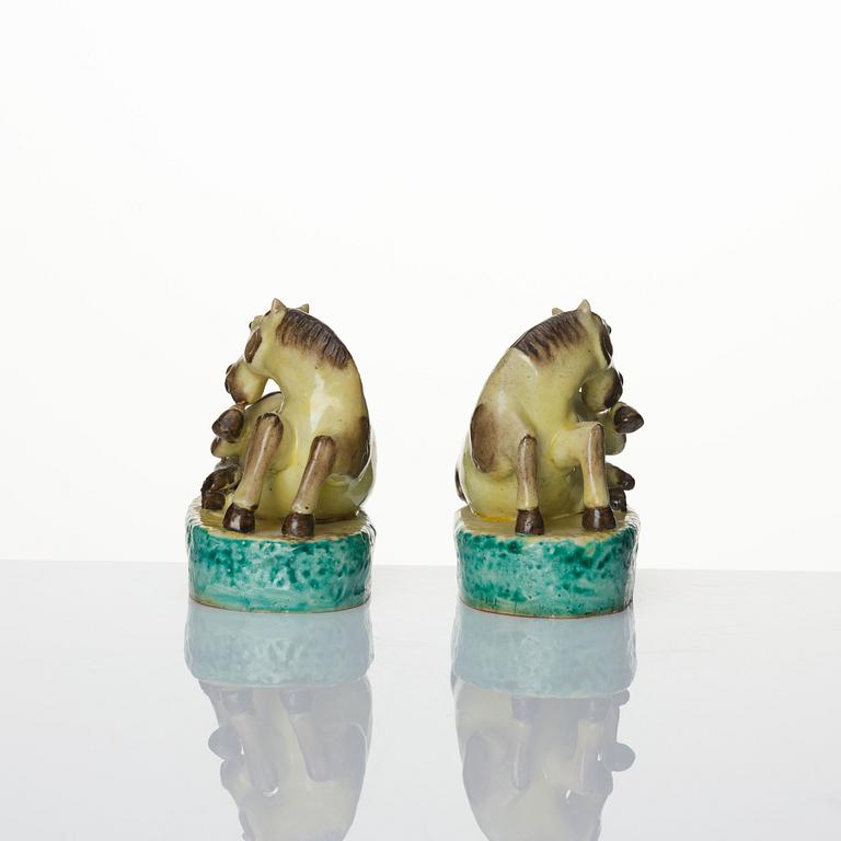 A pair of green, yellow and aubergine glazed biscuit figures of recumbent horses, Qing dynasty.