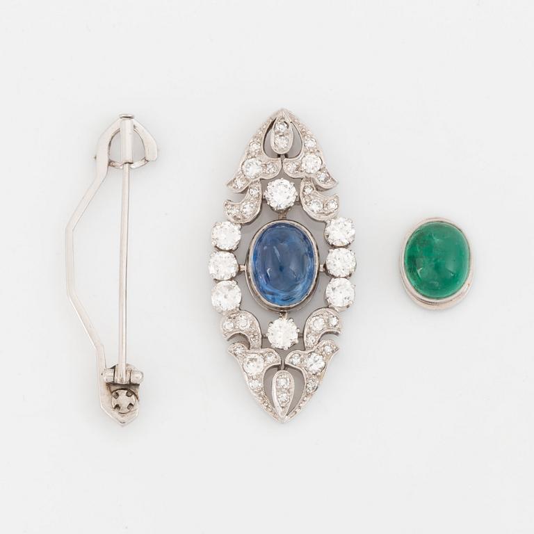 A platinum brooch set with a cabochon-cut sapphire and a cabochon-cut emerald.