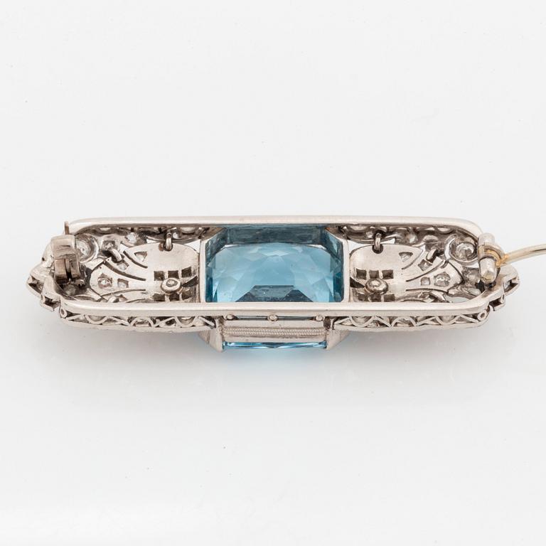 An 18K white gold brooch set with a faceted aquamarine and round brilliant- and rose-cut diamonds.