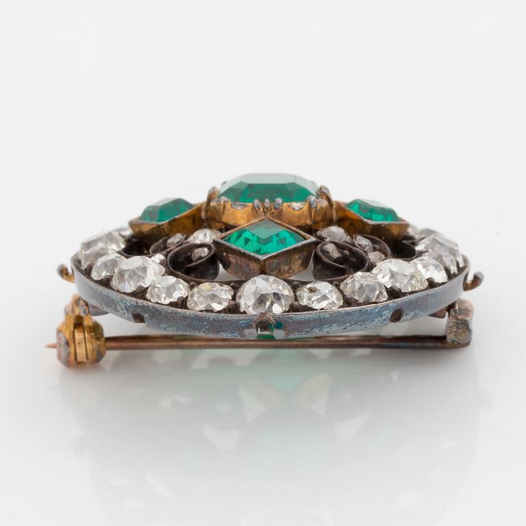 A gold and silver brooch set with faceted emeralds and old- and rose-cut diamonds.