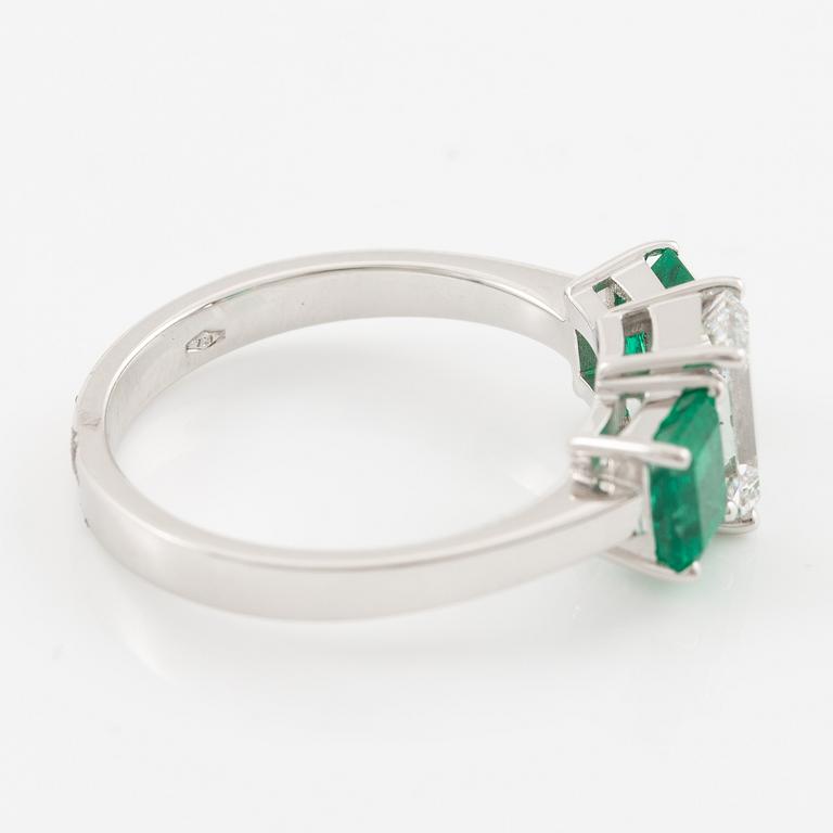 An 18K white gold ring set with an emerald-cut diamond and two step-cut emeralds.