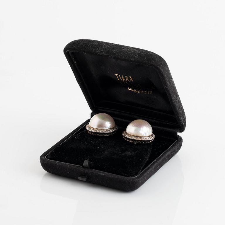 A pair of 18K white gold earrings set with cultured mabe pearls and round brilliant-cut diamonds.